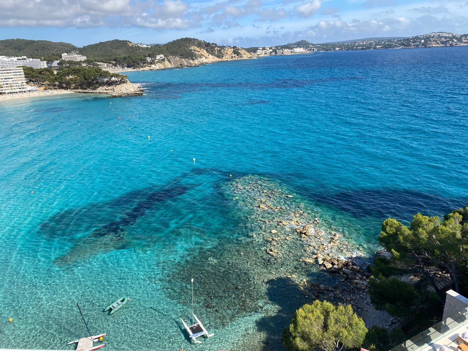 An elevated view of a Mallorcan bay with a sandy beach, clear shallow water and a wooded headland