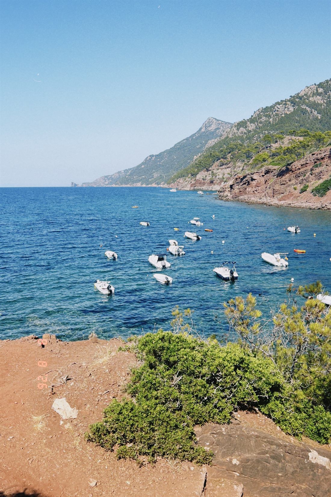 A sheltered Mallorcan bay with moored boats below pine covered hills