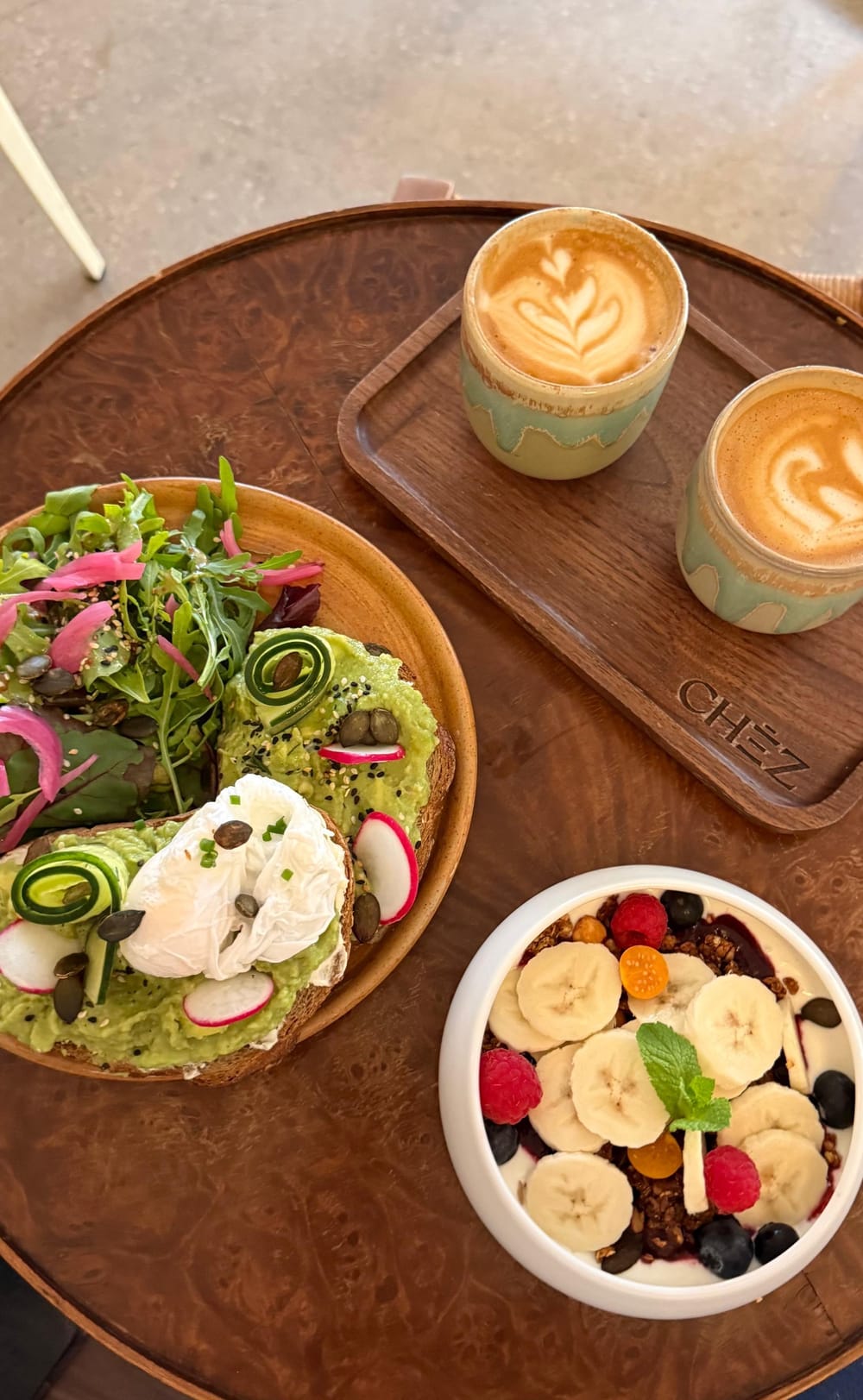 A brunch of salad, fruit and coffee laid out on a round wooden table