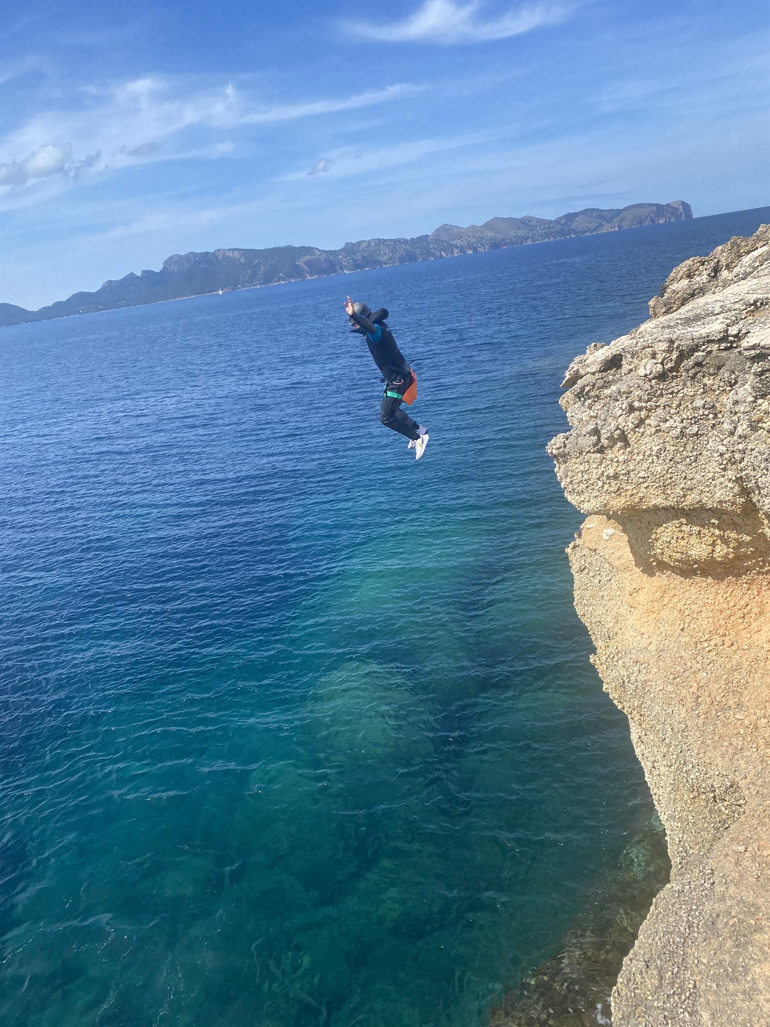 A swimmer in deep turquoise water beneath a limestone cliff on the Mallorcan coast
