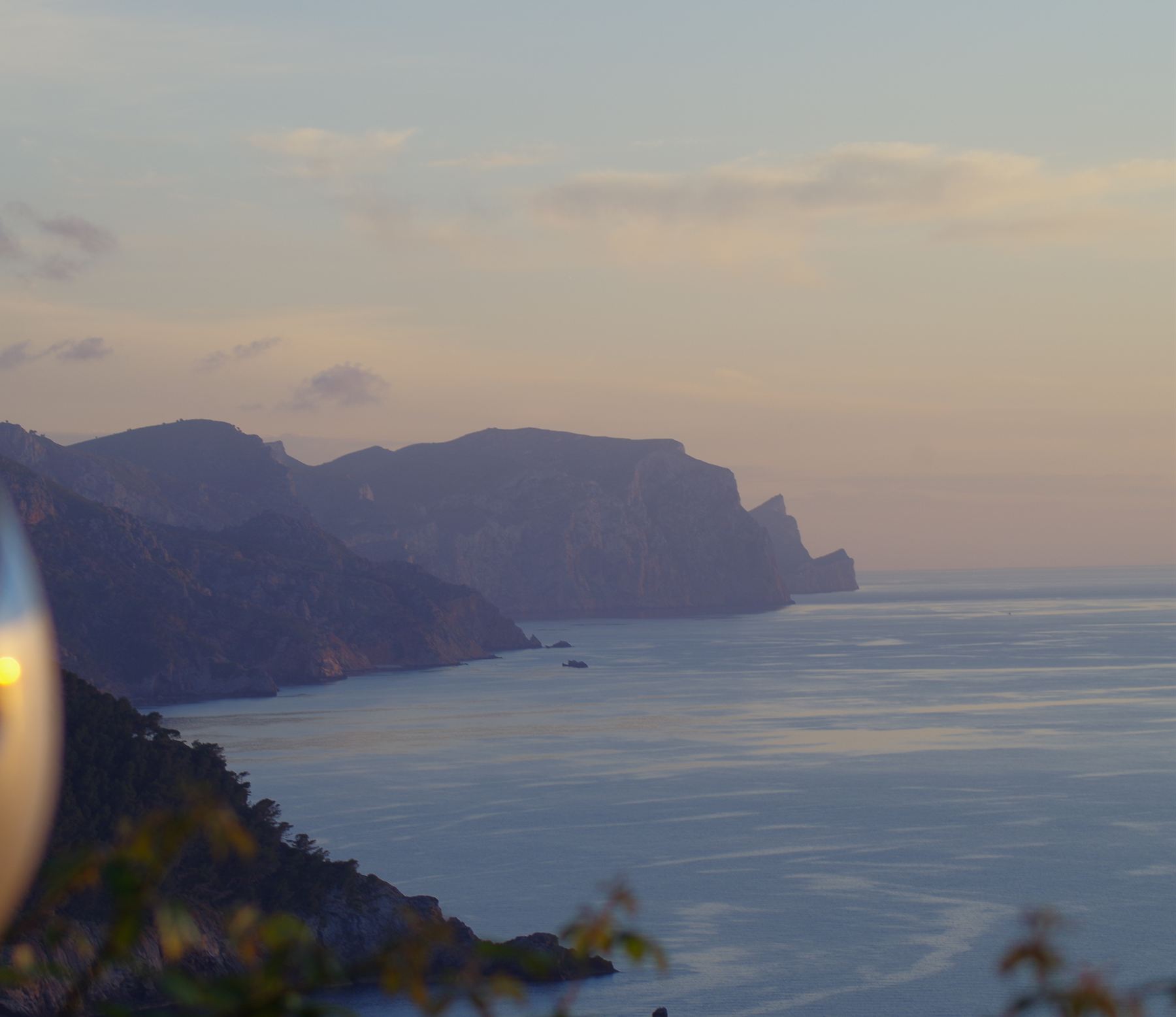 The cliffs of the Serra de Tramuntana receding into haze above a calm sea at dusk